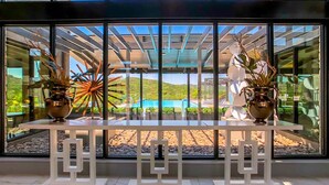 Interior moderno com parede de vidro que oferece vista para uma piscina e paisagem externa.
