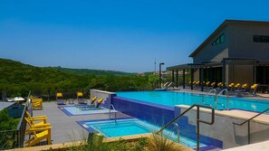 Une piscine sur le toit, avec plusieurs niveaux, des chaises longues jaunes et une vue sur des collines verdoyantes.