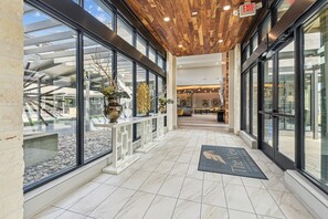 A modern hotel lobby with a glass facade, a wooden ceiling, and a reception desk. - Landing | Incredible 2BD, Gym, Yoga Studio (San Antonio)