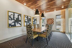 Une salle de conférence avec un plafond en bois, des chaises aux motifs noirs et dorés, et des œuvres d’art abstraites accrochées aux murs.