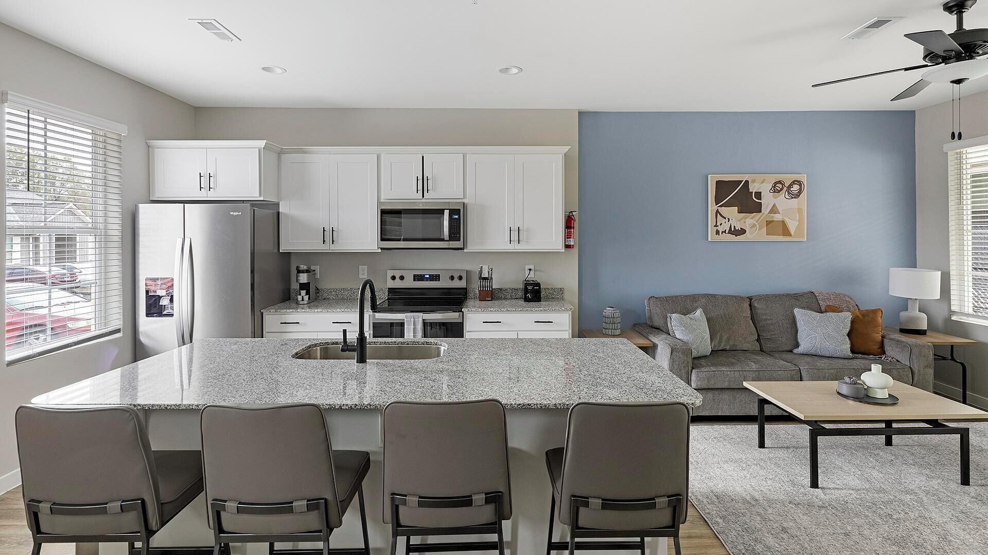 A modern kitchen with white cabinets, a central island with bar seating, and a grey sofa in a living area with a blue accent wall.