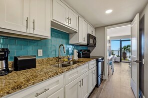 A modern kitchen with white cabinets, a granite countertop, and a view to a balcony. - 🏖️Stunning Ocean Views | Pools | 3BR | Grande Cayman 357🏖️ (Myrtle Beach)