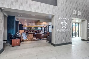 A modern lobby with a reception desk, seating area, and a sign welcoming guests to Grande Cayman Resort.
