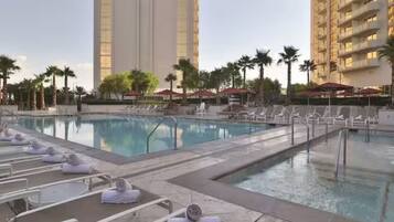 A swimming pool with lounge chairs and towels, surrounded by palm trees and tall buildings.