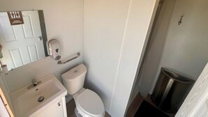 A small, compact bathroom with a toilet, sink, and trash bin.