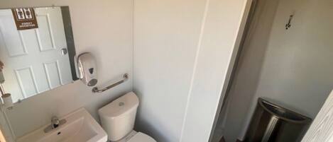 A small, compact bathroom with a toilet, sink, and trash bin.