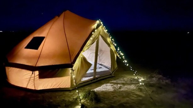 A dome-shaped tent with a window and string lights, set on a snowy surface.