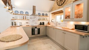 Una cucina moderna con piano di lavoro in legno, forno integrato e microonde. Si nota una parete in mattoni e un soffitto con travi in legno.