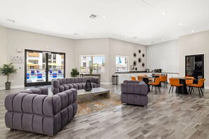 A modern living room with a grey sectional sofa, a coffee table, and a dining area with orange chairs. - Landing | Incredible 1BD, Gym, Clubhouse (Sunrise Manor)