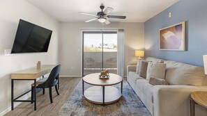 A modern living room with a flat-screen TV, a round table with a decorative item, a sofa, and a ceiling fan. - Landing | Stunning 1BD, Pool, Gym (Sunrise Manor)