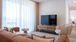 Ein modernes Wohnzimmer mit einem großen Flachbildfernseher, einer Couch, einem Sessel und einem kleinen Beistelltisch.