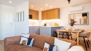 Ein modernes Wohnzimmer mit braunem Sofa, einem Esstisch mit Stühlen und einer Küchenzeile mit Holzschränken und Backofen.