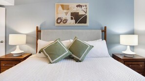 A neatly made bed with two pillows, two bedside tables with lamps, a wall art piece, and a wooden headboard. - Landing | Stylish 1BD, Gym (Las Vegas)