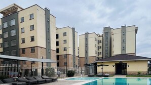 A swimming pool with lounge chairs and a building with multiple floors in the background. - Regal Suites (Athi River)