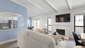Een moderne woonkamer met een open haard, een flatscreen televisie en een keukenhoek met een koelkast.