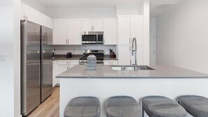 Een moderne keuken met witte kasten, roestvrijstalen apparatuur en een centraal eiland met barkrukken.