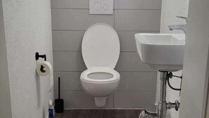 A modern bathroom with a toilet, a sink, and a toilet paper holder. - 3-bed Cosy Apartment - Sleeps 7 (Villingen-Schwenningen)
