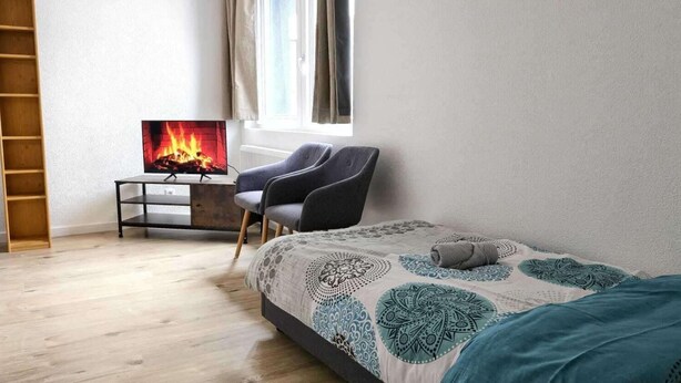 A bedroom with a bed, a TV, a chair, and a wooden ladder. - 3-bed Cosy Apartment - Sleeps 7 (Villingen-Schwenningen)