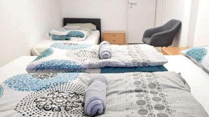 A hotel room with two beds, each with patterned bedding and a rolled towel. There is a chair and a small table in the room. - 3-bed Cosy Apartment - Sleeps 7 (Villingen-Schwenningen)