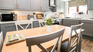 A modern kitchen with grey cabinets, a wooden dining table, and a vase with flowers. - Dolly Blue (Ulverston)