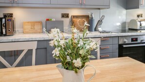 A modern kitchen with grey cabinets, a wooden cutting board, a microwave, and a vase with white flowers on the counter. - Dolly Blue (Ulverston)