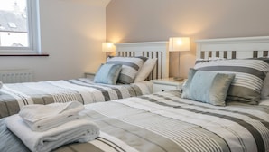 A hotel room with two beds, striped bedding, bedside lamps, and a window with a view of buildings. - Dolly Blue (Ulverston)