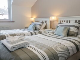 Habitación de hotel con dos camas, ropa de cama a rayas, lámparas de noche y ventana con vistas a edificios.