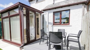 A patio with a table and chairs, a sliding glass door, and a white exterior wall. - Dolly Blue (Ulverston)