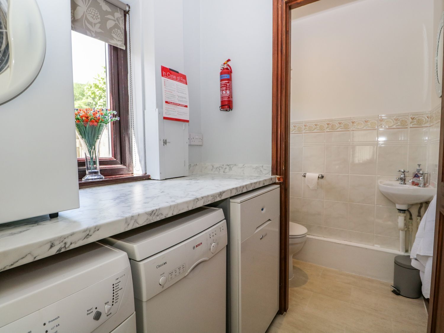 A compact kitchen with a dishwasher, a sink, and a toilet visible in the adjacent bathroom.