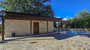A stone building with a wooden door, a covered patio, and a swimming pool area.
