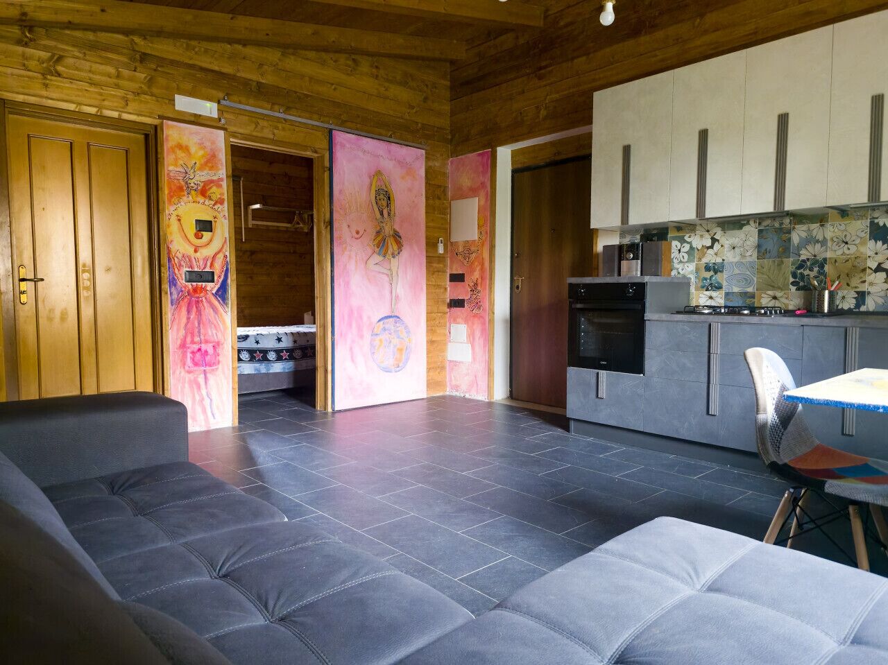 Un intérieur moderne avec un canapé gris, une cuisine dotée d’un mur de crédence carrelé et un plafond en bois.