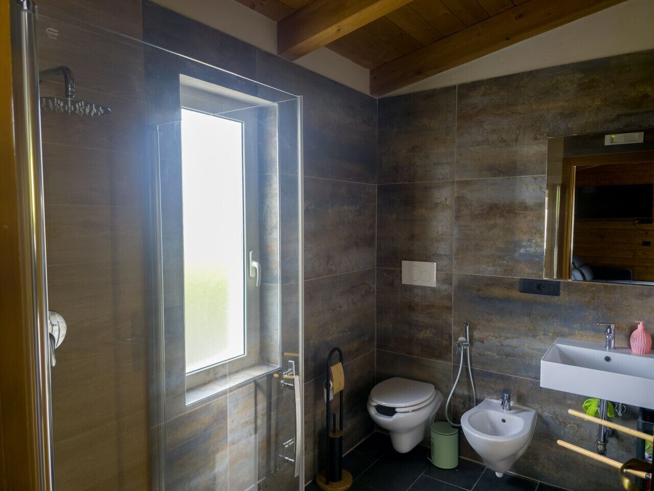 A modern bathroom with a glass shower enclosure, a toilet, a bidet, and a sink.