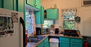 Une cuisine avec des meubles de couleur turquoise, un réfrigérateur, un évier, une cuisinière et une fenêtre avec des rideaux.