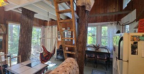 Een rustiek houten interieur met een hangmat, een houten trap, een eettafel, stoelen en een koelkast.