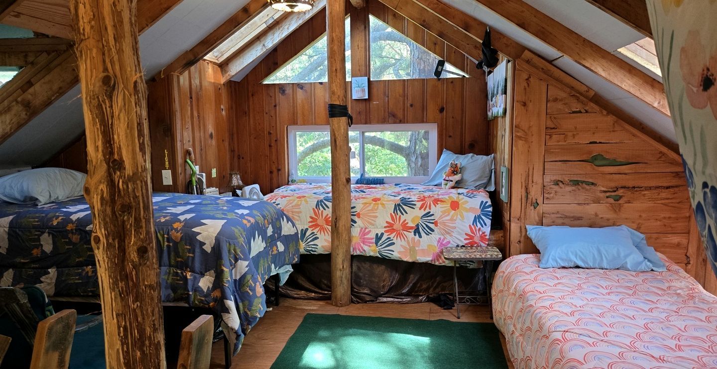 Une chambre mansardée chaleureuse avec des murs en bois, deux lits, une petite table et une fenêtre.
