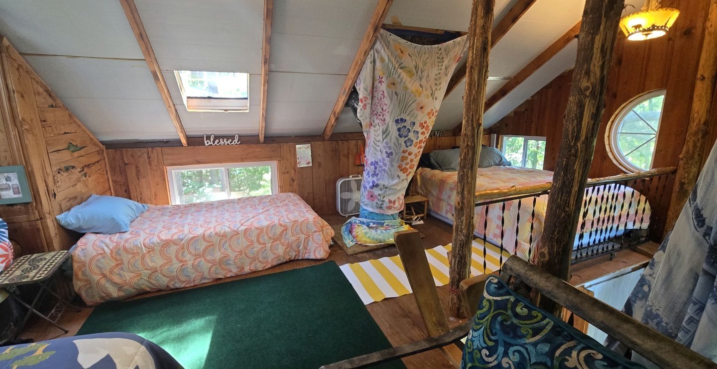 A cabin with a loft bed, a lower bunk bed, a small table, and a window.