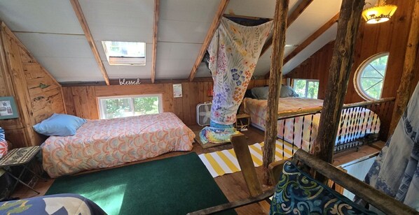 A cabin with a loft bed, a lower bunk bed, a small table, and a window.