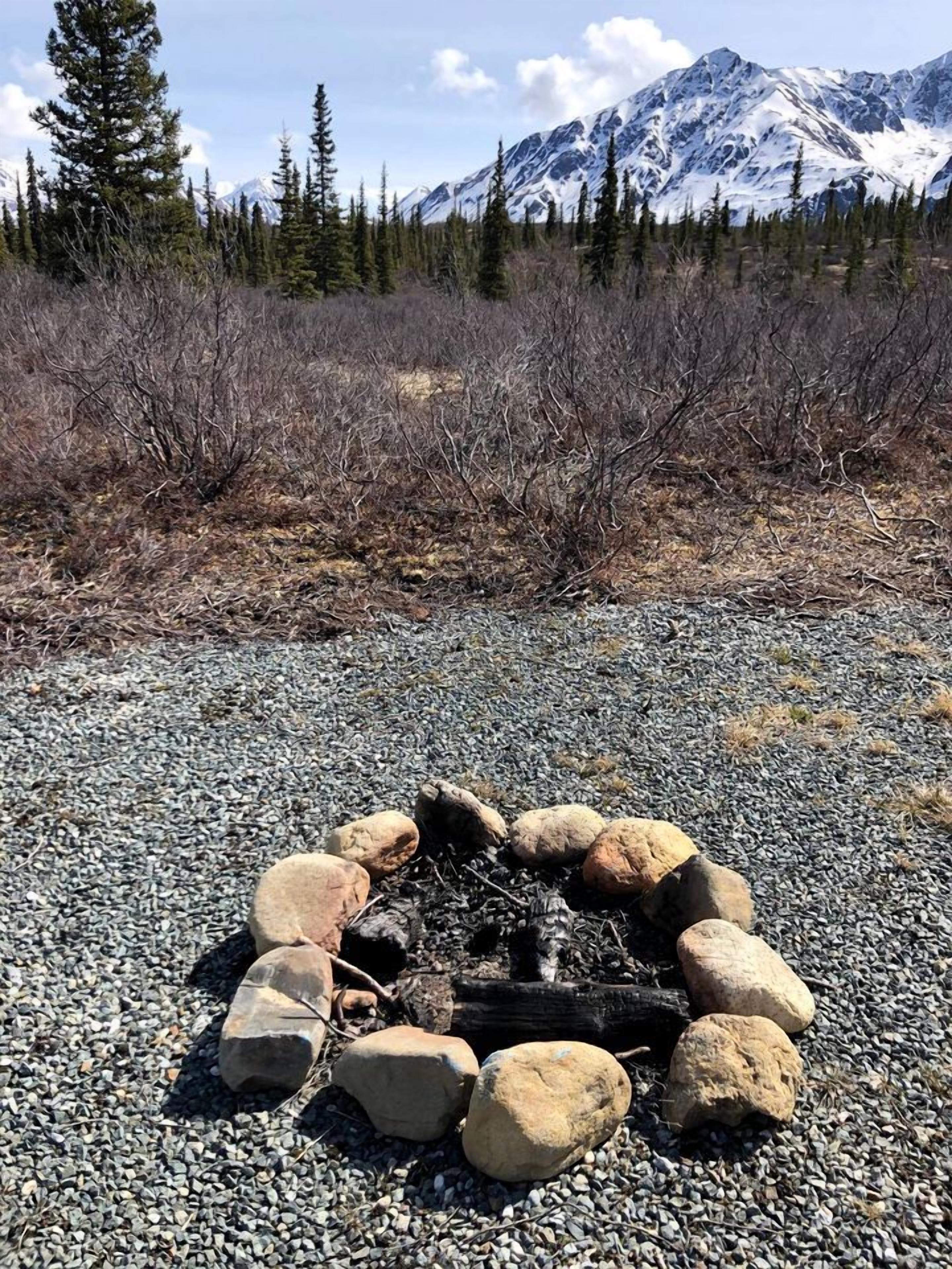 A fire pit surrounded by rocks on a gravel surface with a mountainous landscape in the background.