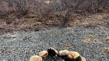 A fire pit surrounded by rocks on a gravel surface with a mountainous landscape in the background.