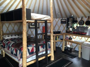 A yurt with a bunk bed, a small kitchen area with cooking utensils, and a dining table.