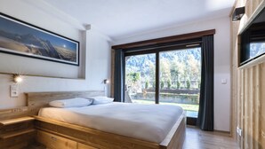 Ein Schlafzimmer mit einem hölzernen Bett, einem Nachttisch, einem großen Fenster mit Bergblick und einem gerahmten Bild an der Wand.