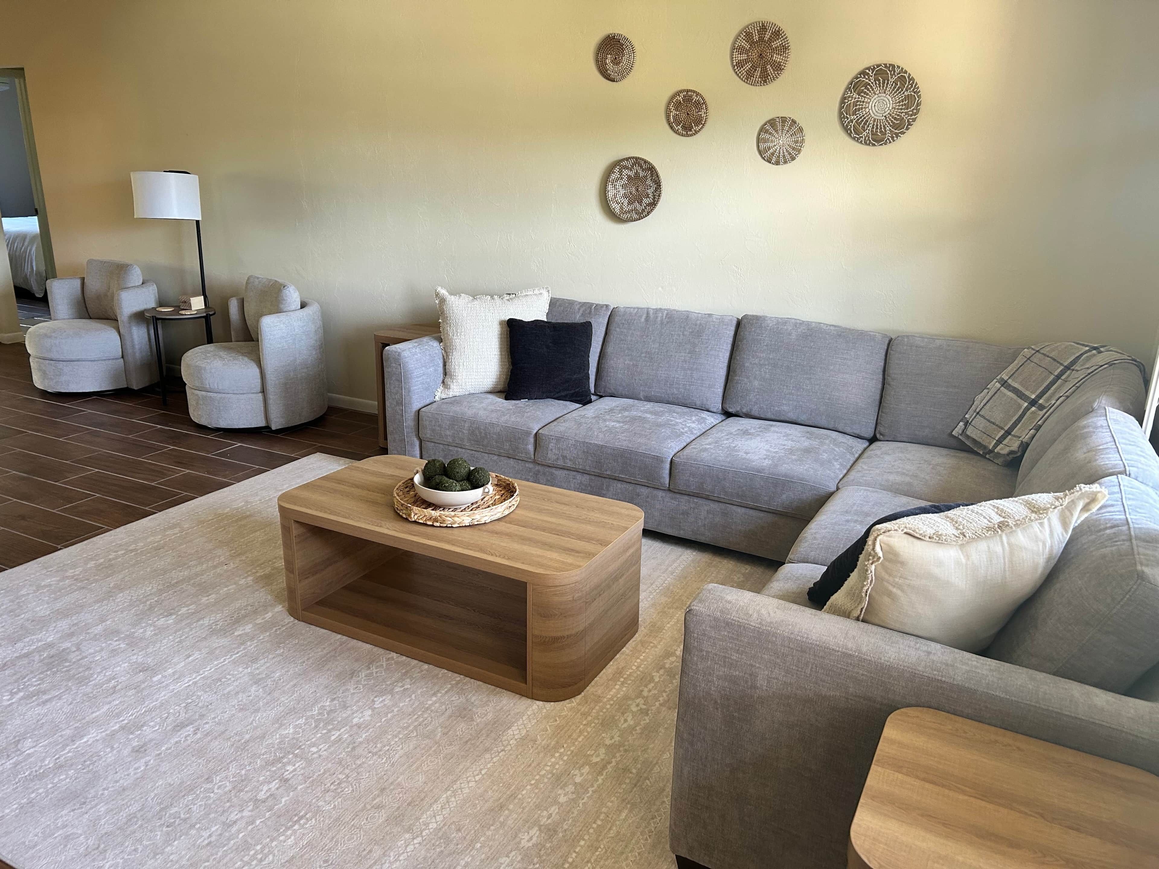 A modern living room with a grey sofa, a wooden coffee table, and a patterned rug.