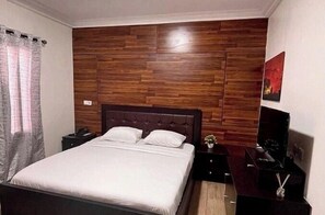 Een slaapkamer met een houten paneelwand, een bed met wit beddengoed, een nachtkastje, een televisie en een aan de muur hangend kunstwerk.