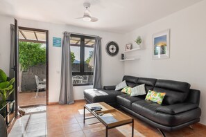 Ein Wohnzimmer mit einer Ledersofa, einem Couchtisch, einem Fernseher und einem Fenster mit Vorhängen.