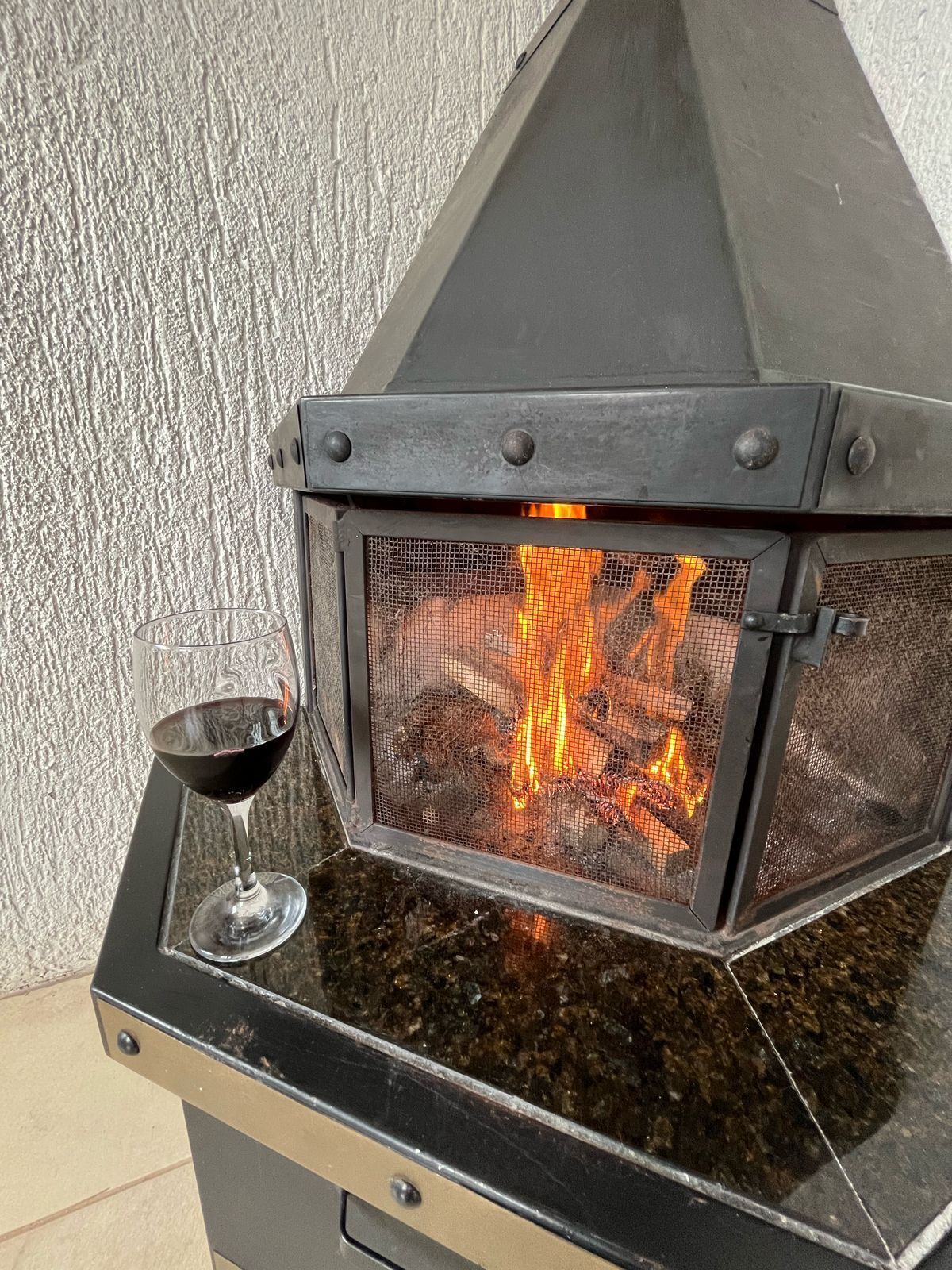 A glass enclosure with a fire inside, placed on a table with a glass of red wine beside it.