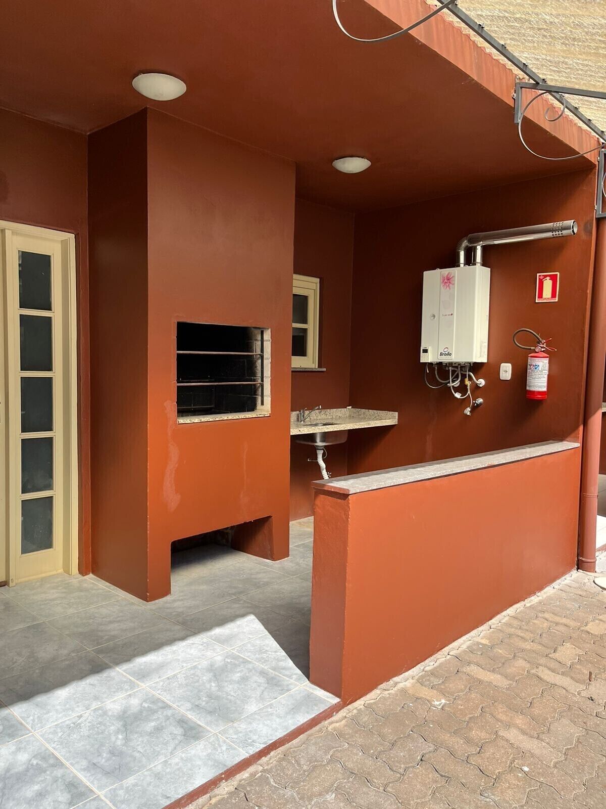 A restroom with a tiled floor, a sink, a window, and a fire extinguisher.