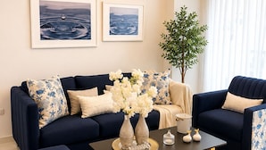 A modern living room with a dark blue sofa set, a coffee table with decorative items, and a large window with sheer curtains. - Tropical Apartment with Pool | Hemingay Beach | TEPUY Juan Dolio (Playa Juan Dolio)