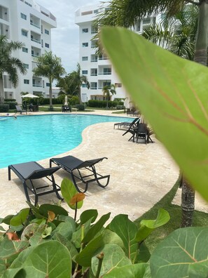 Piscina com espreguiçadeiras e um edifício ao fundo.