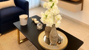 A modern living room with a flat-screen TV mounted on a wooden wall, a dark sofa, a coffee table with decorative items, and sheer curtains. - Tropical Apartment with Pool | Hemingay Beach | TEPUY Juan Dolio (Playa Juan Dolio)