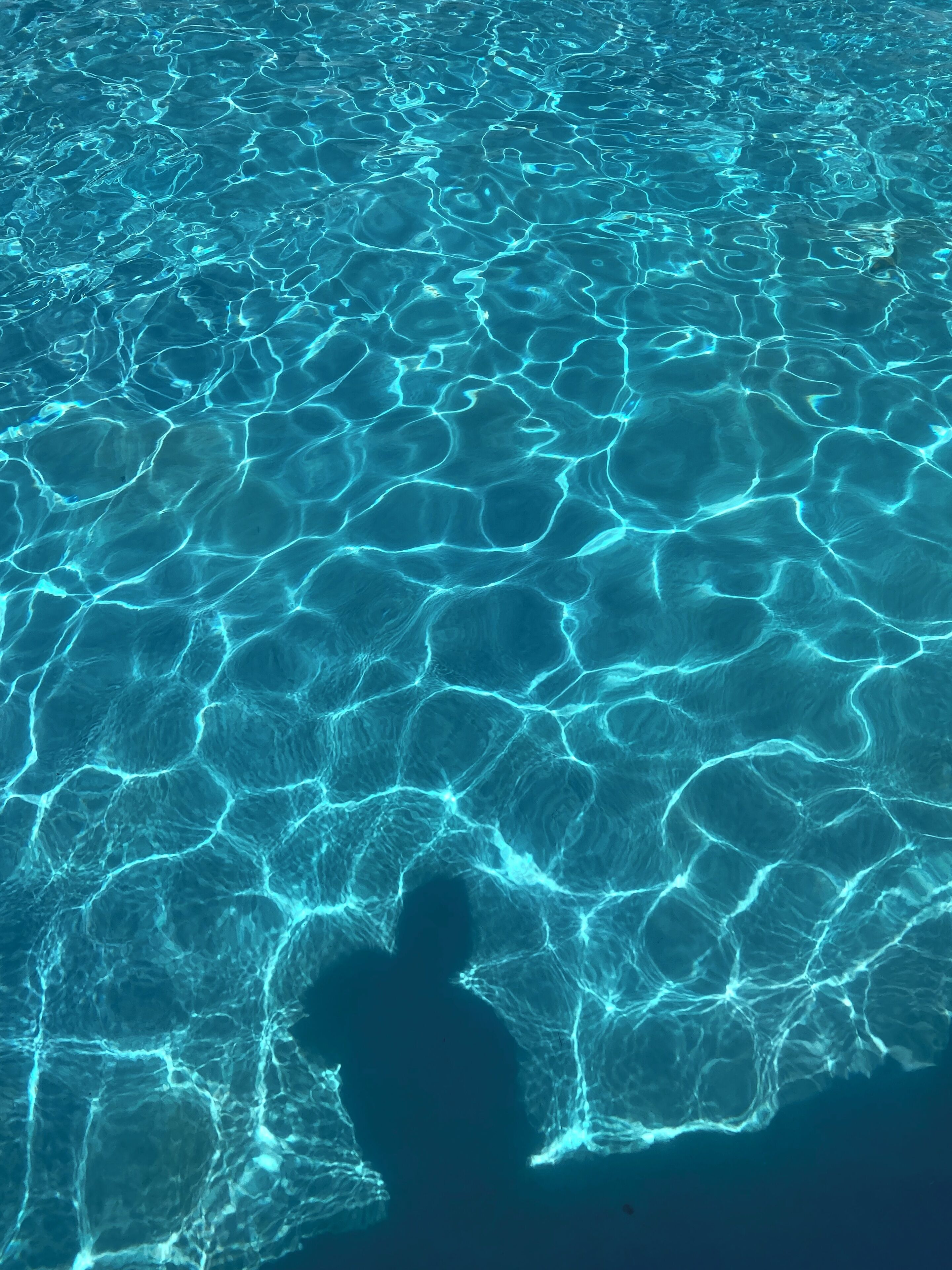 A pool with clear, rippling water and a visible shadow of a person.